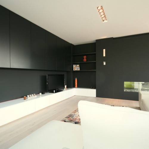 In deze woonkamer zorgden we ervoor dat de kleur van de hangkasten volledig identiek was aan die van de muren. Onderaan geeft het witte contrast een oplichtend effect aan  de living . Kast-ID Antwerpen